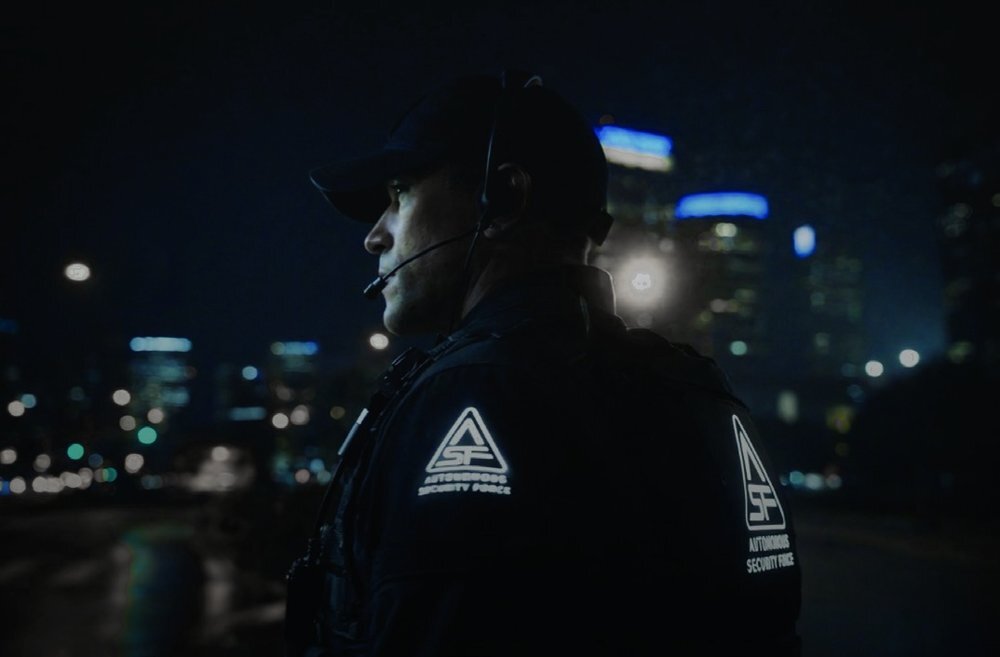 A Knightscope licensed security agent wearing the Autonomous Security Force patch, on post at night in a city